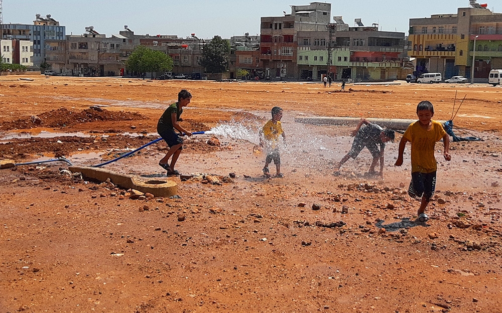 Sıcaktan bunalan çocuklar çamurda halay çekip hortumla serinledi